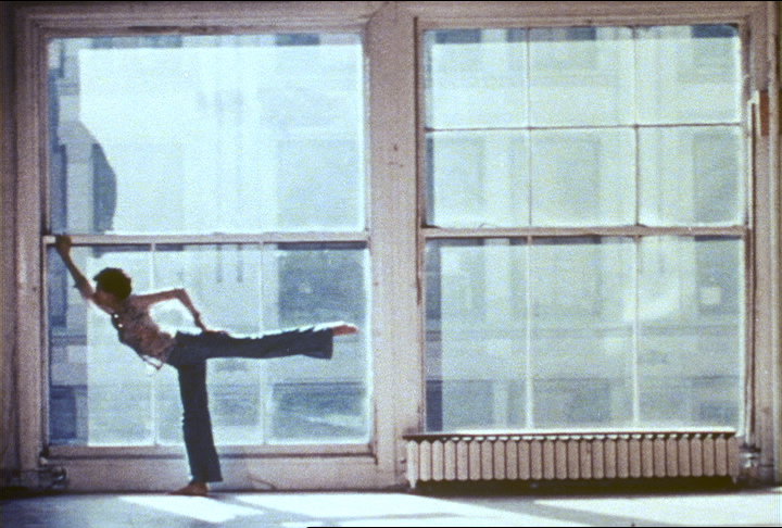 Matt Turney doing an arabesque in the lower left part of a larg loft window. Film still from Windows in the Kitchen, filmdance by Elaine Summers, courtesy the Jerome Robbins Dance Division, the New York Public Library for the Performing Arts